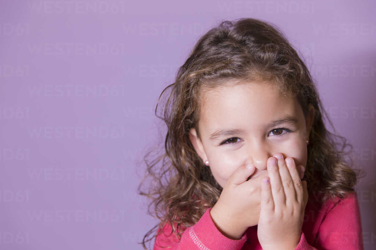 Portrait Of Laughing Little Girl Covering Mouth With Her Hands Stock Photo