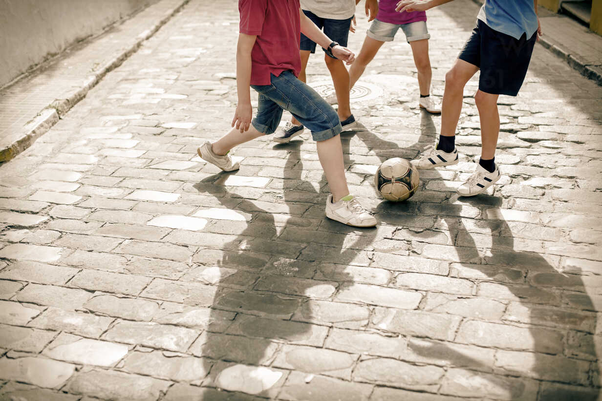 Kinder spielen mit Fußball auf einer Straße mit Kopfsteinpflaster, lizenzfreies Stockfoto