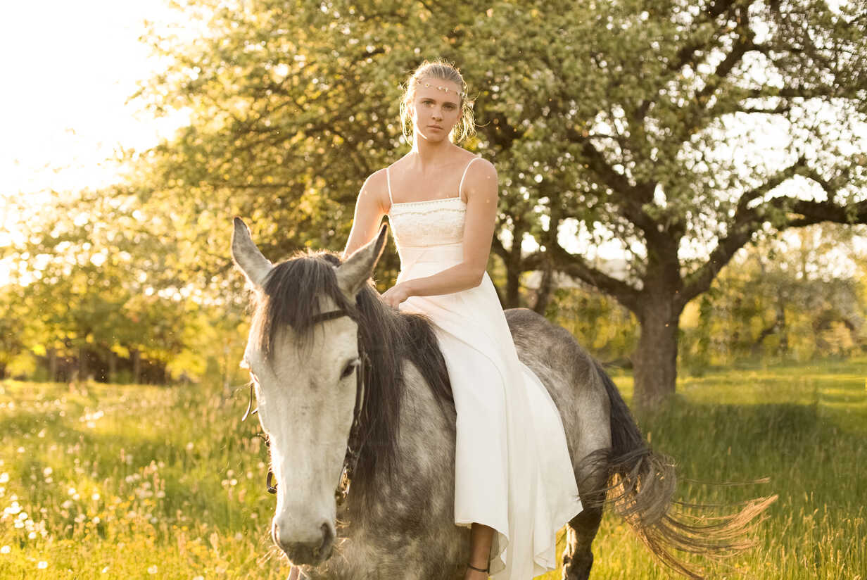 Beautiful young woman riding horse, wearing white summer dress ...