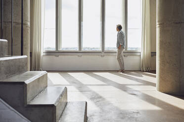 Senior man looking out of window in a loft flat stock photo