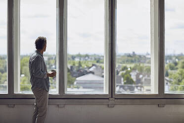Senior man looking out of window in a loft flat stock photo